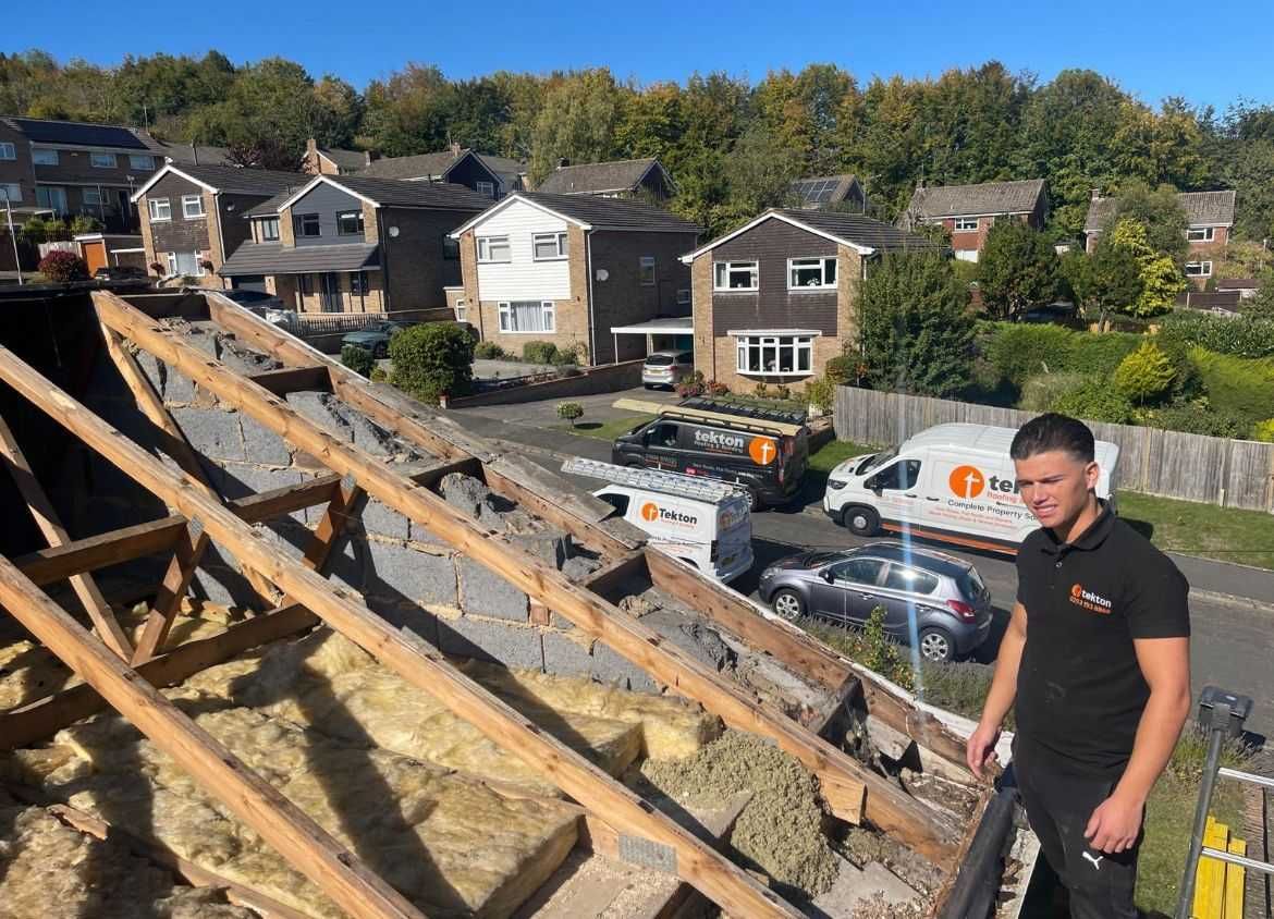 Man on a roof with exposed insulation and wooden beams. A van and houses are in the background.