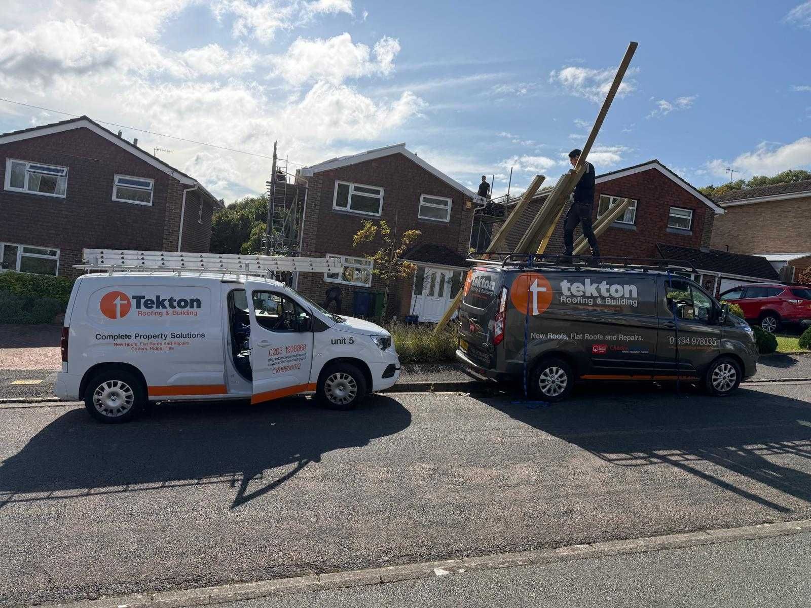 Two Tekton vans parked, one with door open. A person balances wooden planks on a roof. Suburban street.
