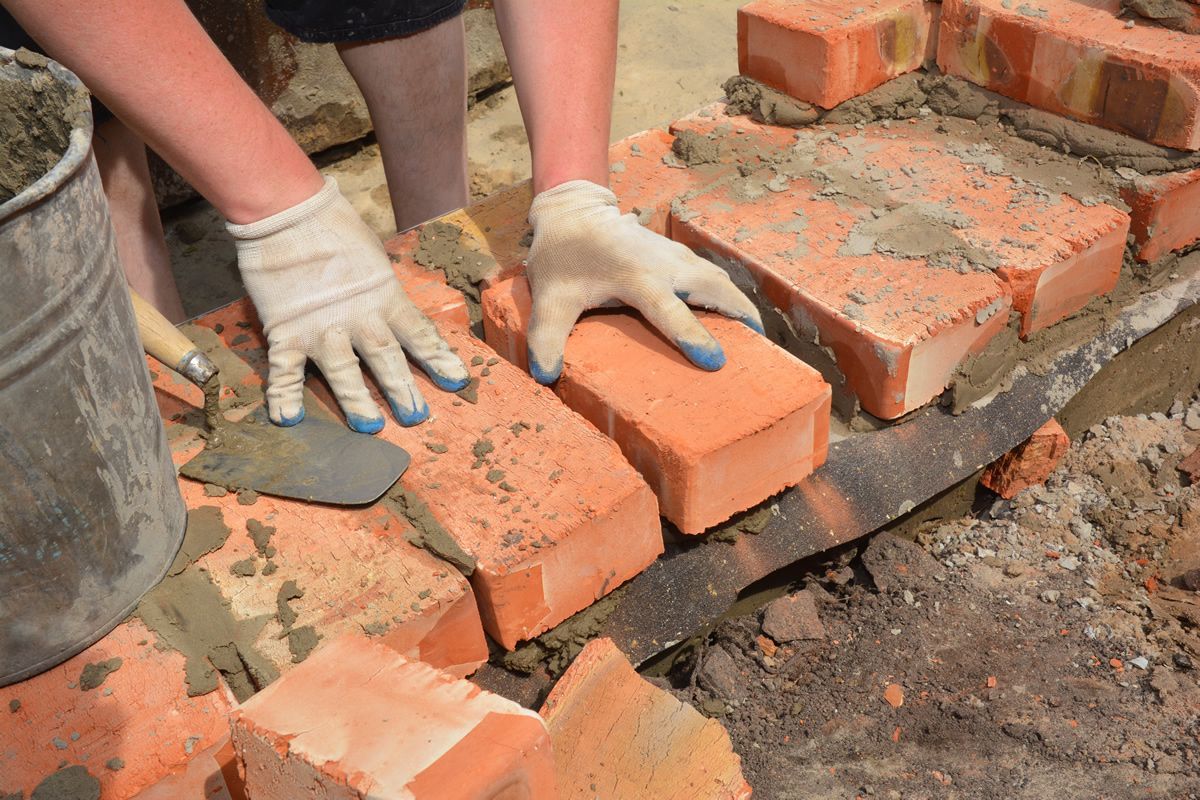 Person in gloves laying red bricks with mortar.