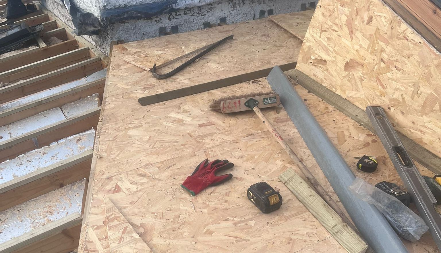 Construction materials and tools on a wooden surface, including a saw, gloves, and measuring tape.
