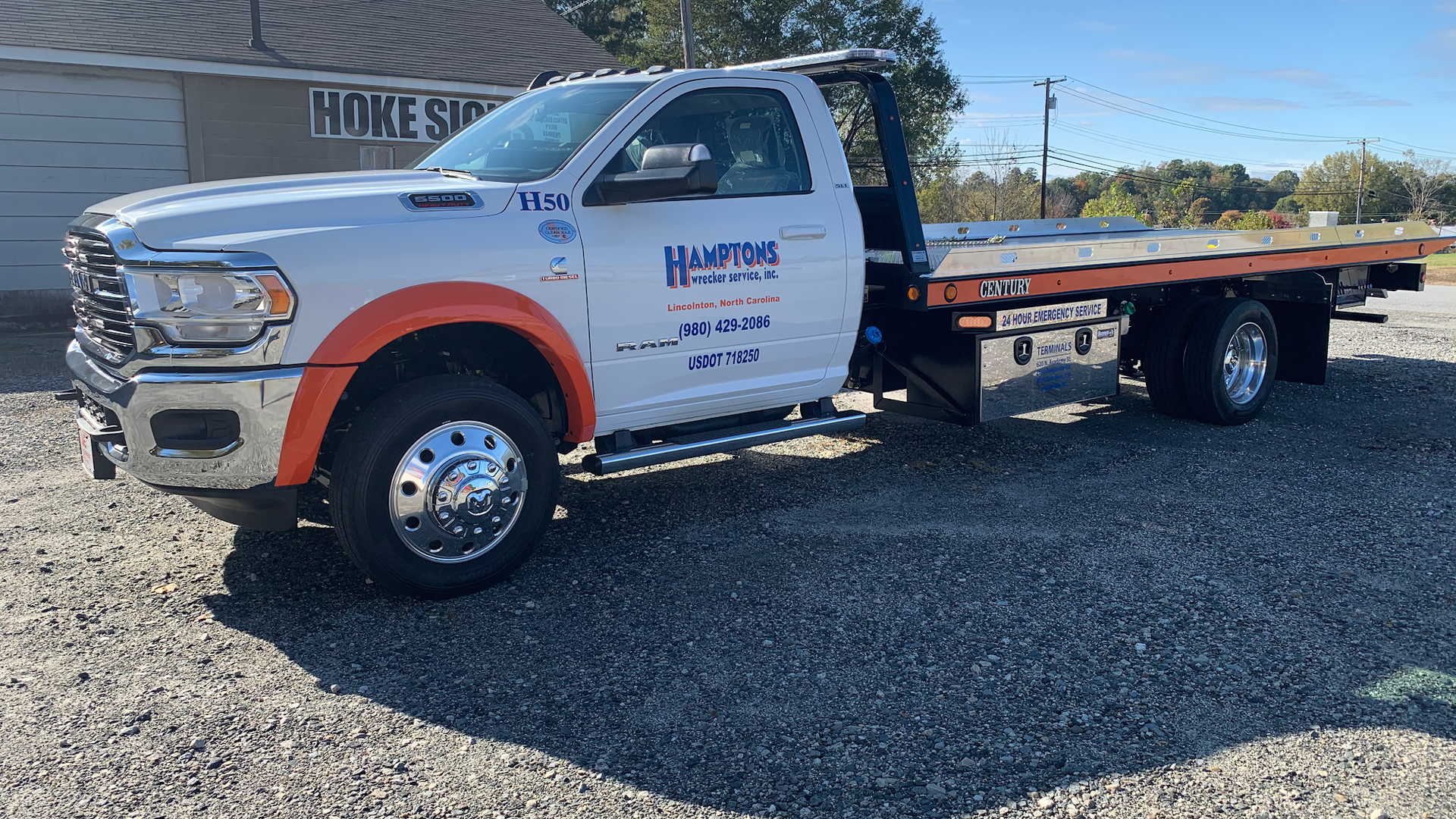White tow truck with orange accents parked on gravel in front of a building.