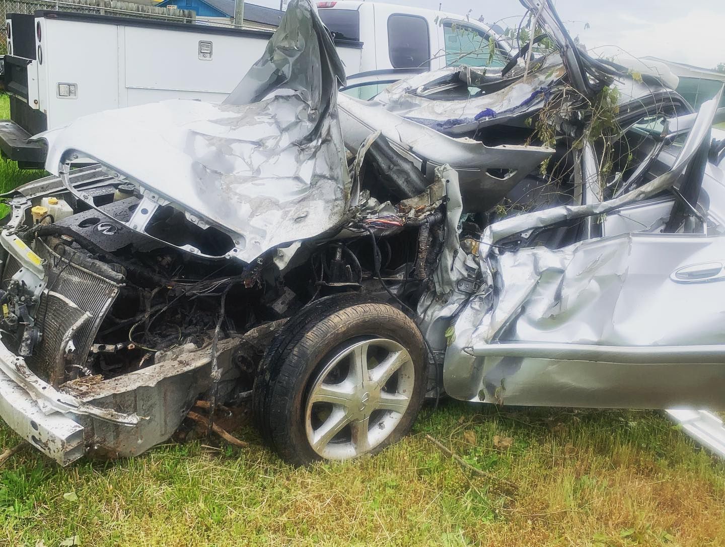 Severely damaged silver car after a major crash. The front and side are crushed, showing extensive damage.