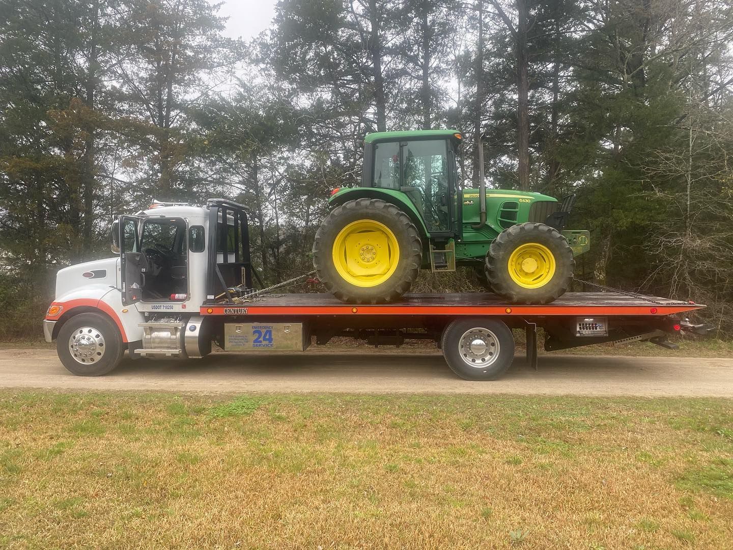 Tow truck carrying a green and yellow tractor on a dirt road.
