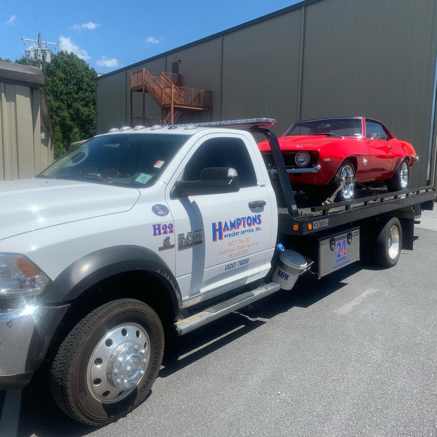 A red classic car is being towed on a flatbed truck. The truck is white with 