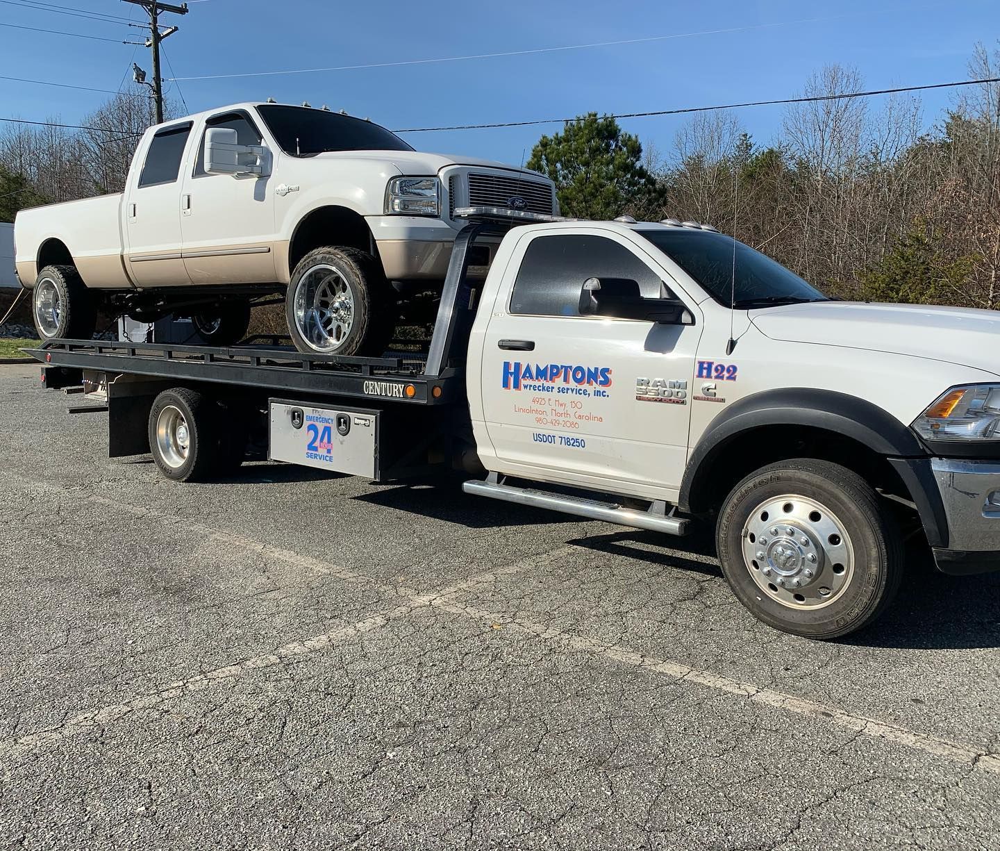 A white pickup truck on a flatbed tow truck, both parked on gravel. The tow truck has 