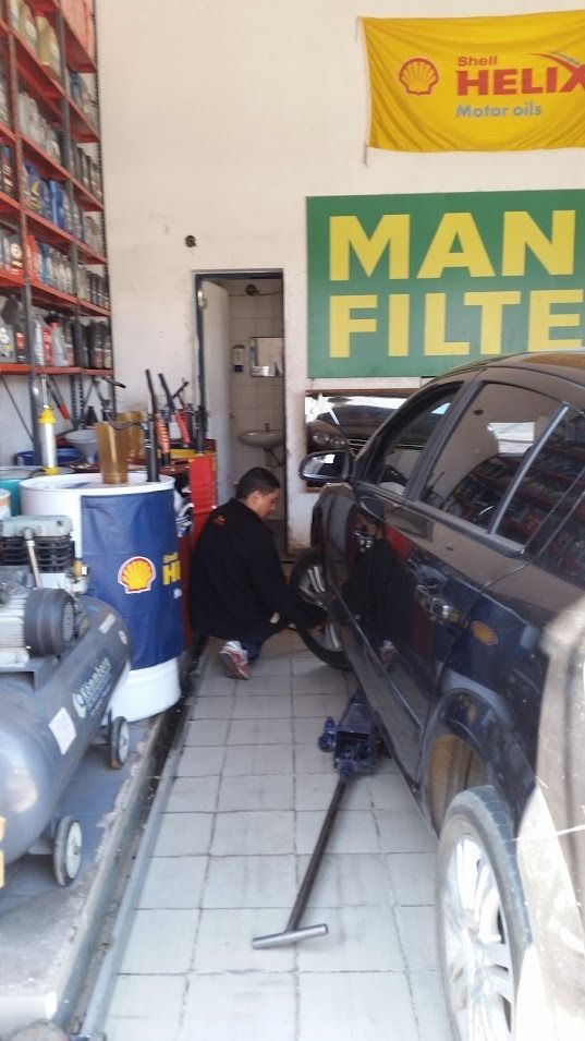 Mecánico trabajando en un SUV oscuro en un garaje junto a un compresor de aire azul y un letrero de MAN FILTER.