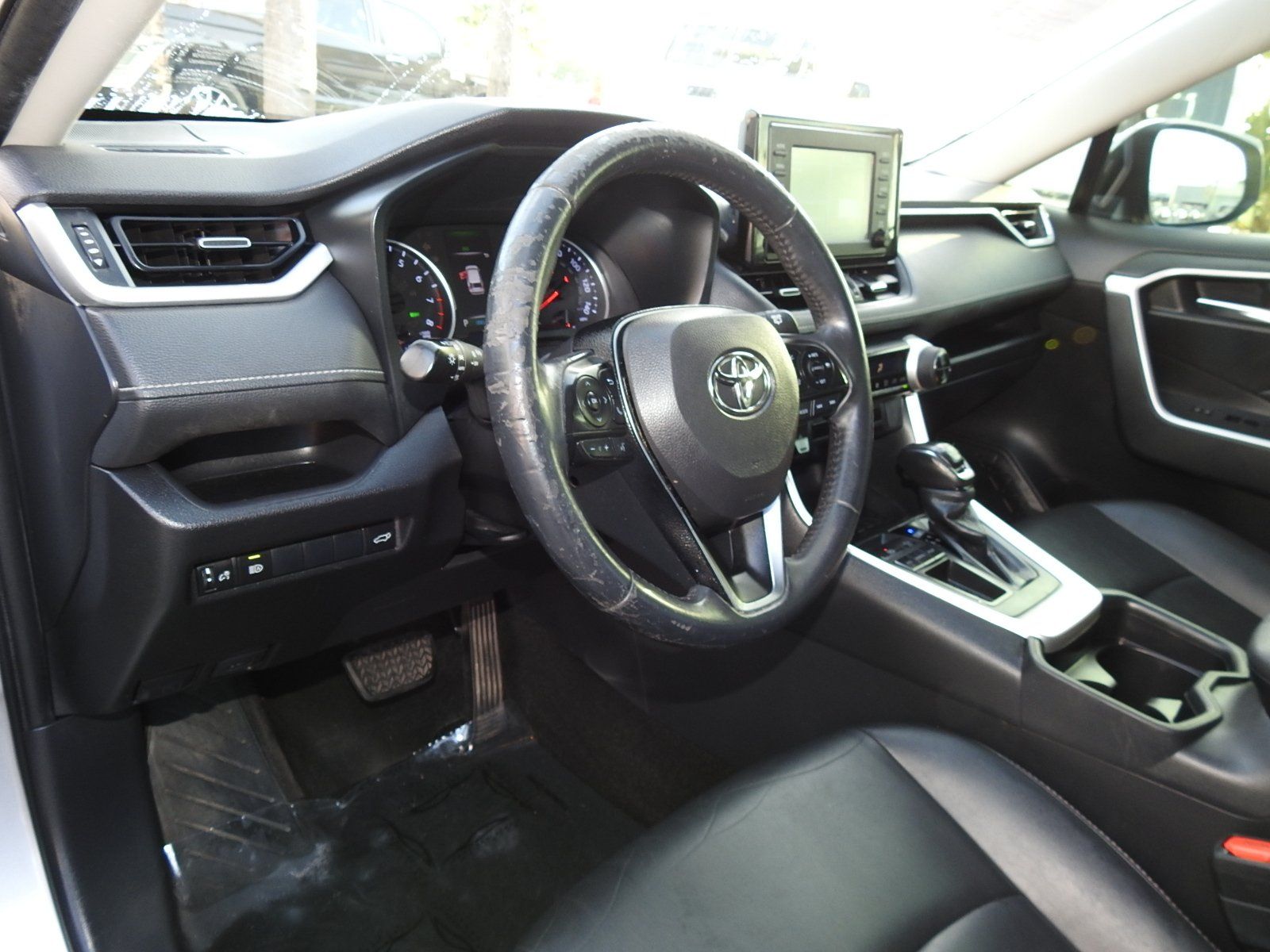 A driver's side view of a Toyota RAV4 interior, featuring a black steering wheel, dashboard, and leather seats.