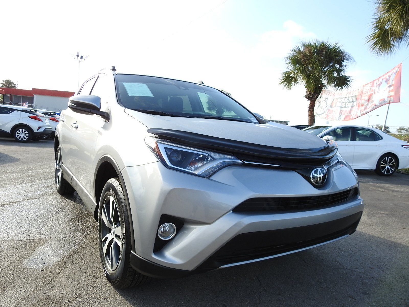 A silver Toyota RAV4 parked at a car dealership on a sunny day.