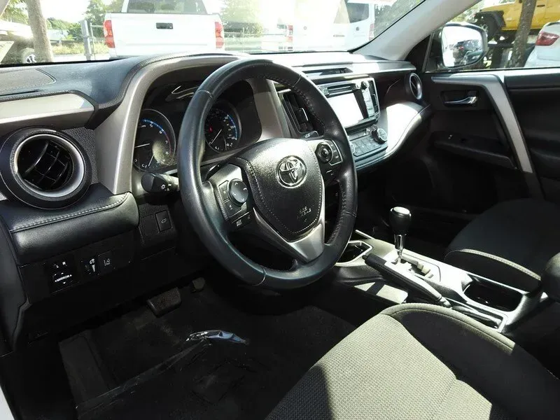 Interior view of a black Toyota RAV4 cockpit, featuring the steering wheel, dashboard, gear shifter, and cloth seats.