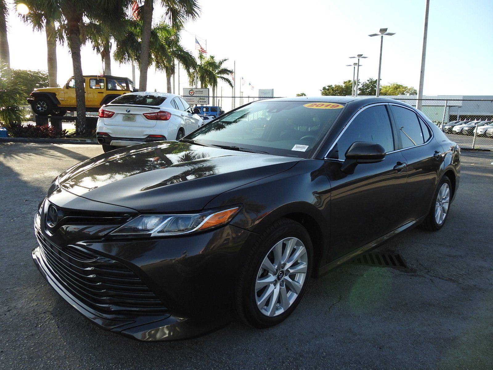 A dark-colored Toyota Camry parked in a dealership lot during the day, with other vehicles visible in the background.