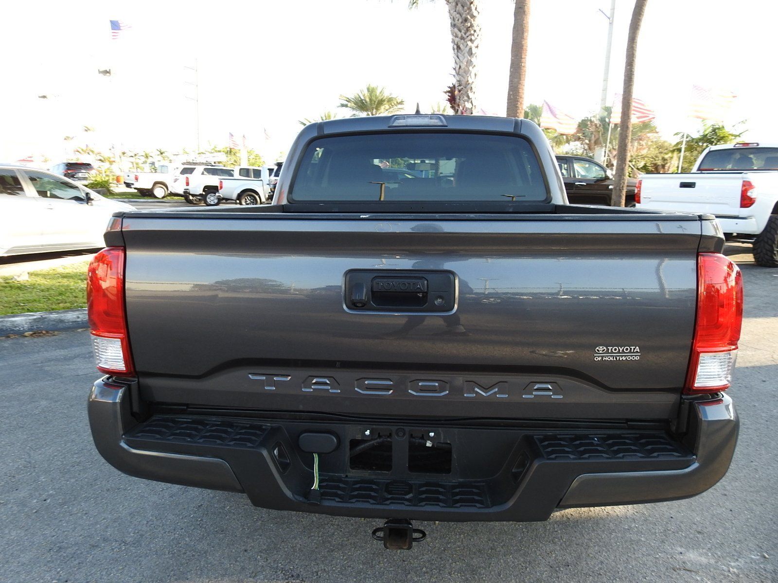 The back view of a dark gray Toyota Tacoma pickup truck parked in a car dealership lot.