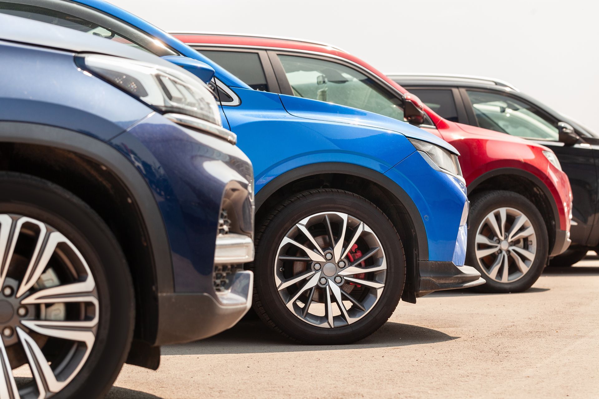 Row of parked SUVs in blue, red, and black, shown from the side in a car lot