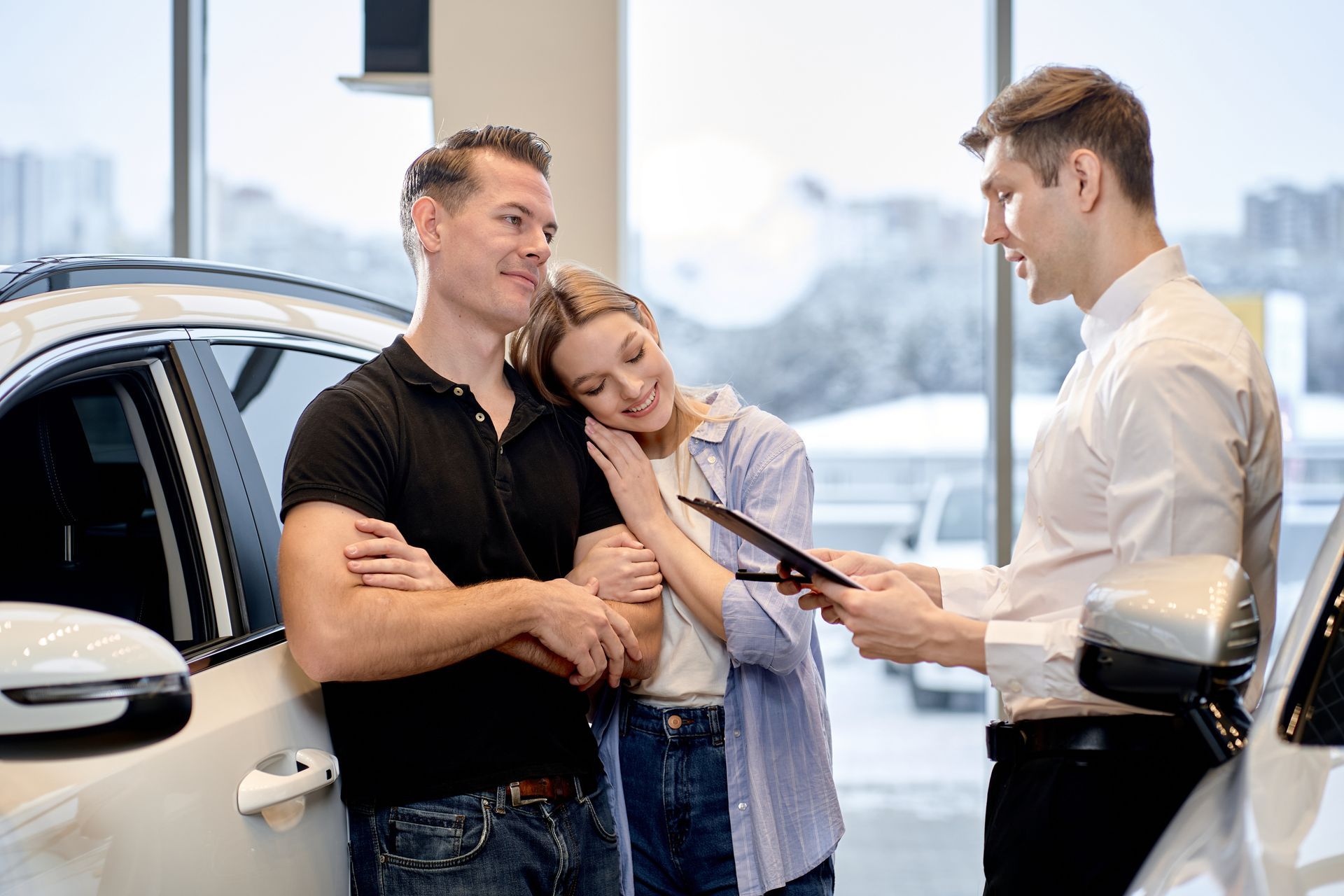 Salesperson showing paperwork to a couple beside a white car in a dealership
