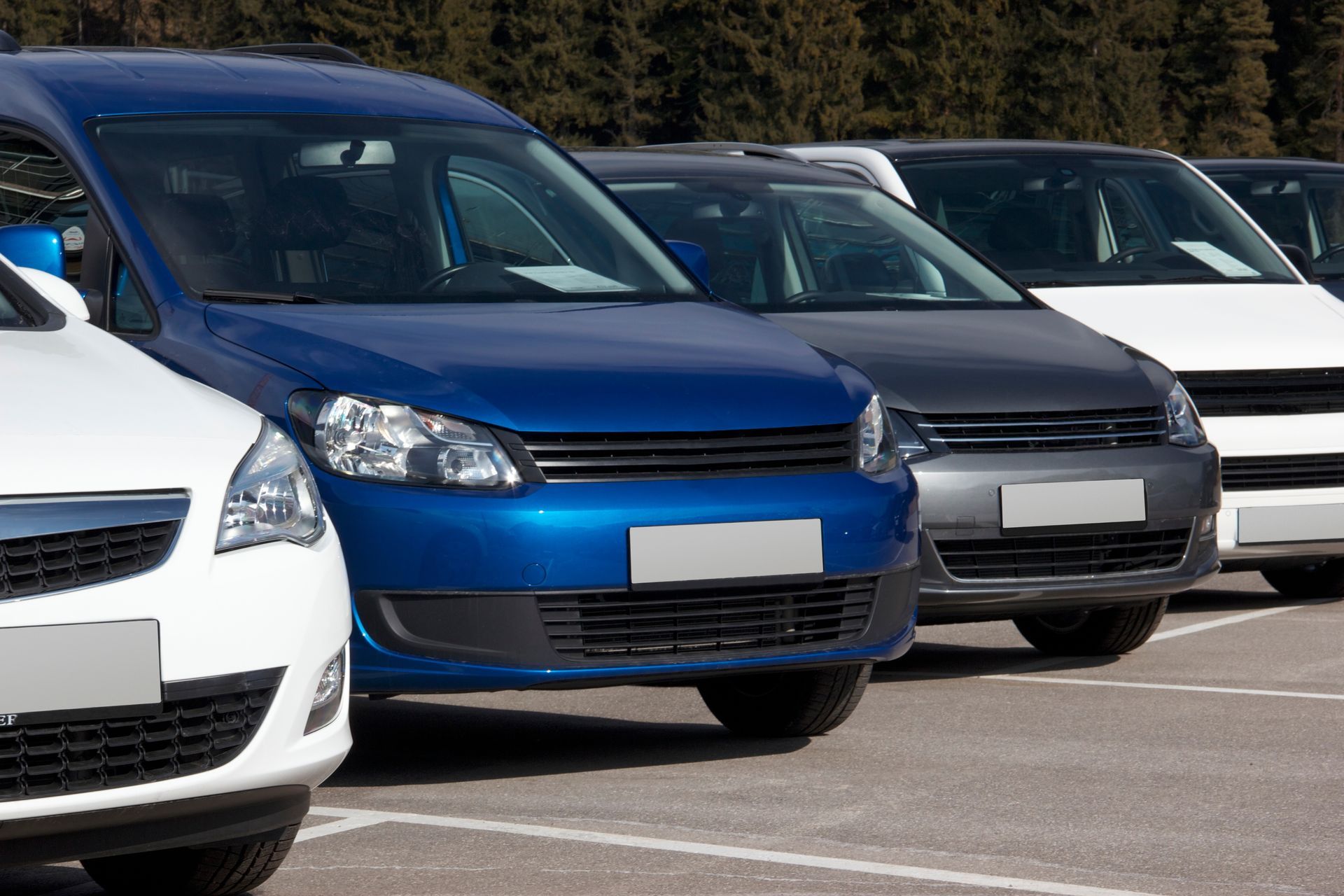 Row of parked cars in a lot, including a blue car in the foreground and white and gray cars рядом