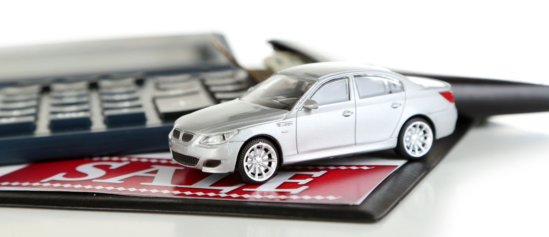 Toy silver sedan on a calculator with a credit card and laptop keyboard in the background