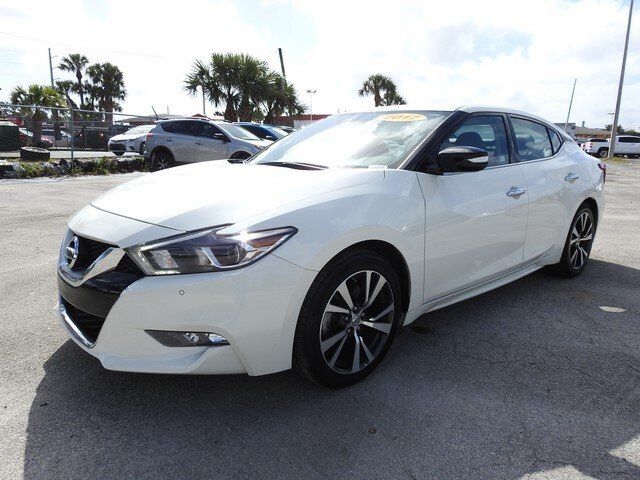 A white Nissan Maxima parked on a paved lot on a sunny day.
