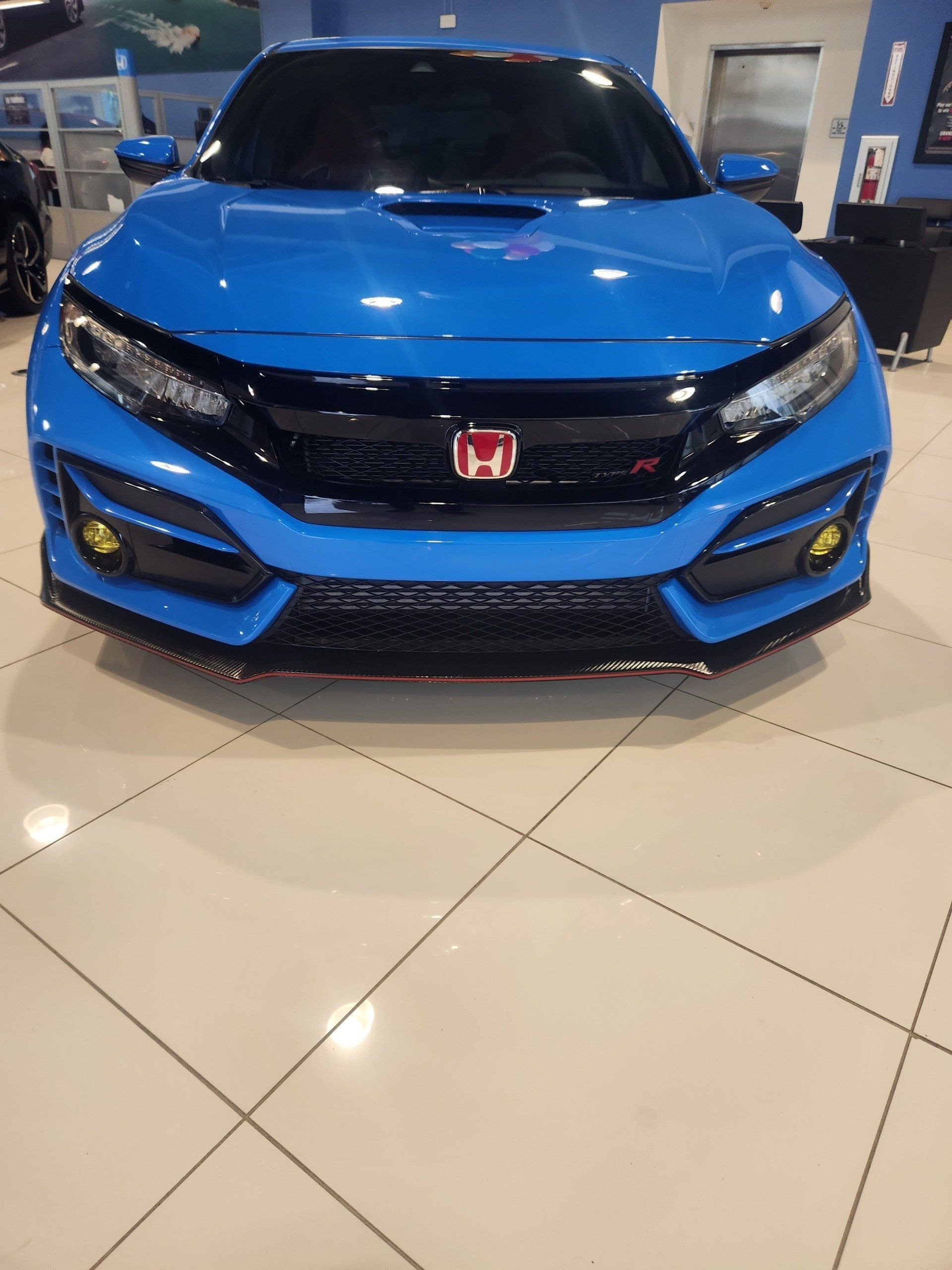 A bright blue Honda Civic Type R displayed in a showroom with tile flooring.