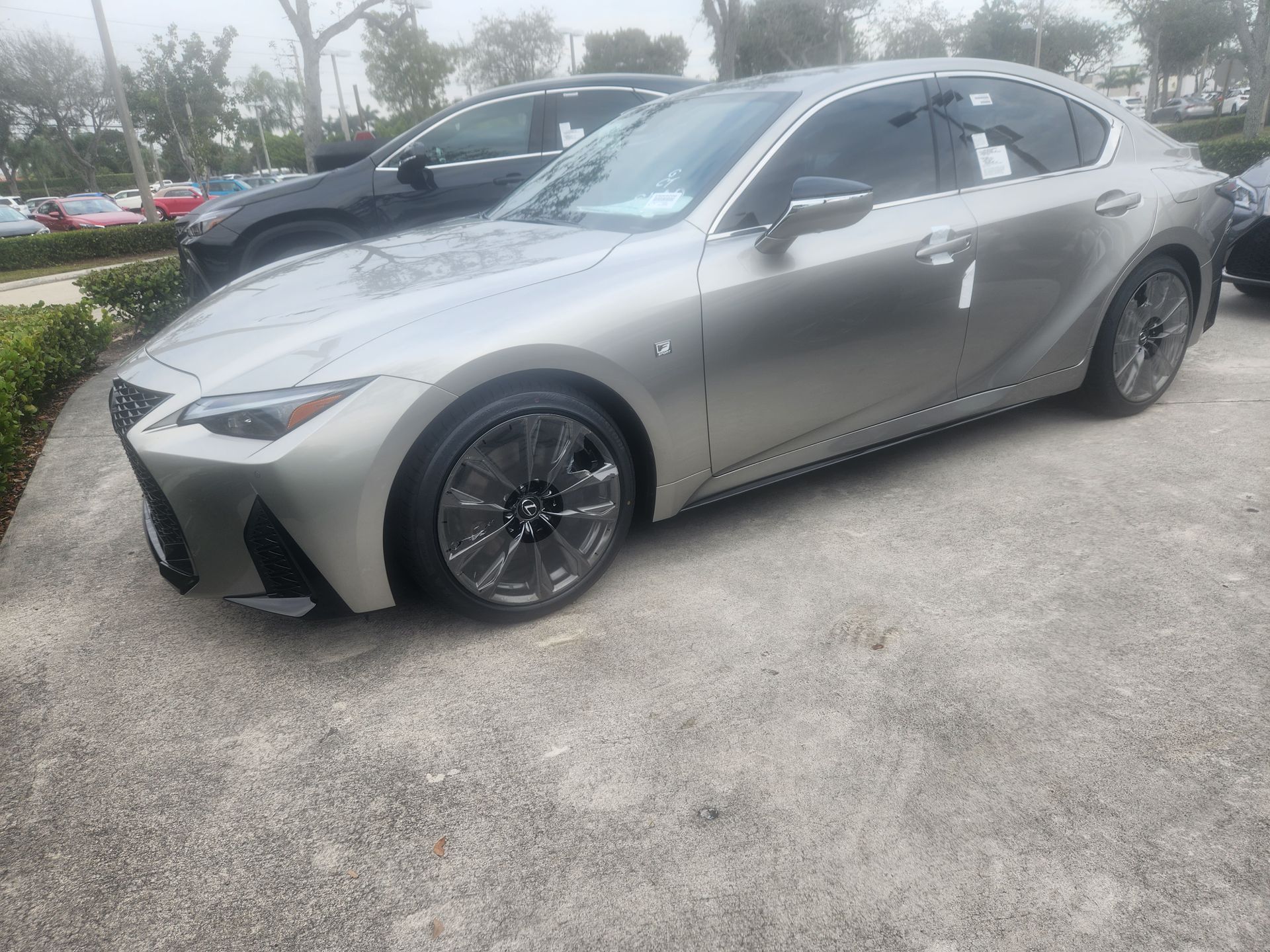 A silver Lexus IS sedan parked on a concrete lot on a bright, hazy day.