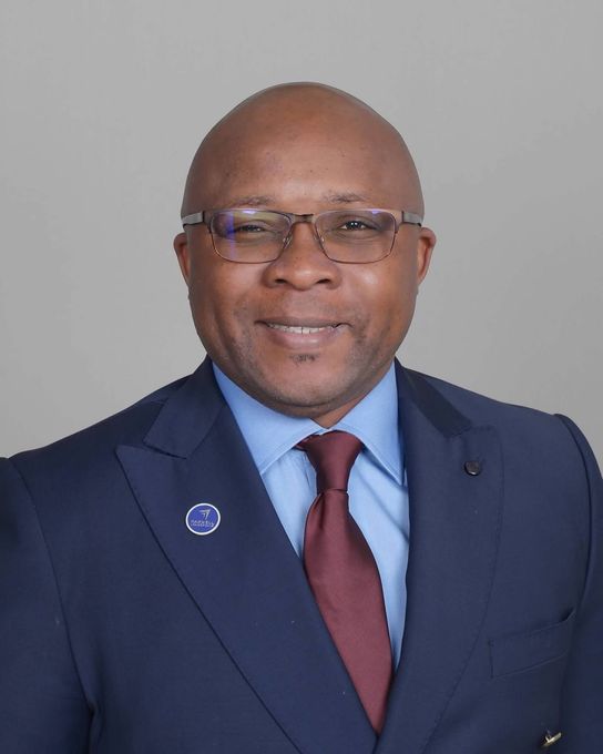 Portrait of a man in a navy suit, blue shirt, red tie, and glasses against a gray background.
