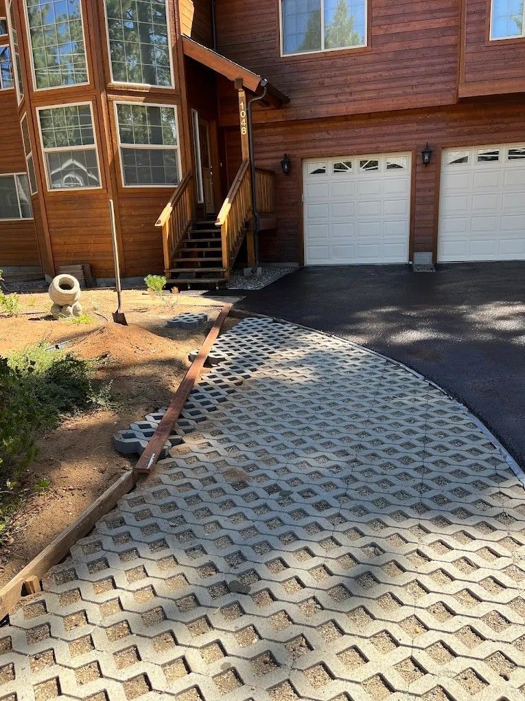 House exterior with two garage doors, wooden siding, and a patterned driveway leading to the entrance