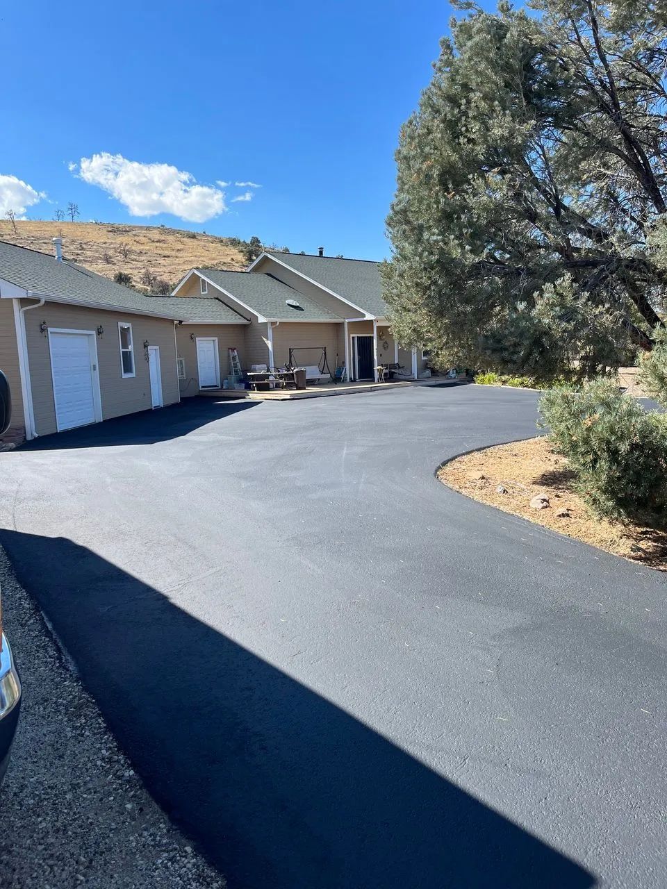 Suburban house with garage doors and a curved blacktop driveway under a blue sky