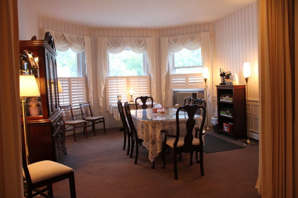 A dining room with a large table set for a meal, windows with white curtains, and antique furniture.