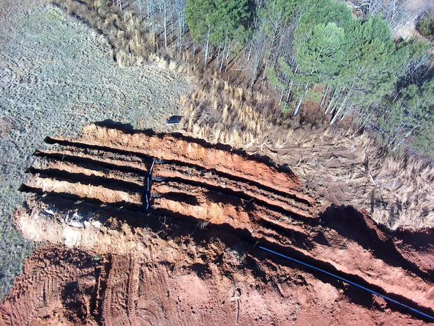 Aerial view of layered red rock cliffs beside sparse trees and rocky ground