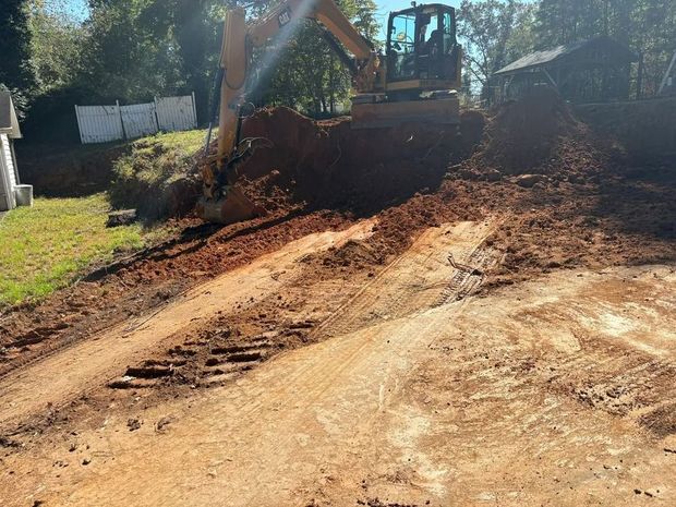 Bulldozer grading a dirt slope on a sunny hillside with trees in the background