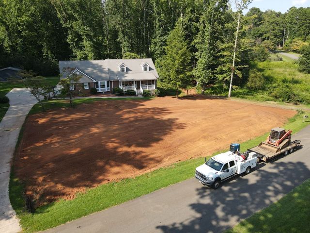 White truck with trailer on a large cleared yard beside a house and trees, viewed from above