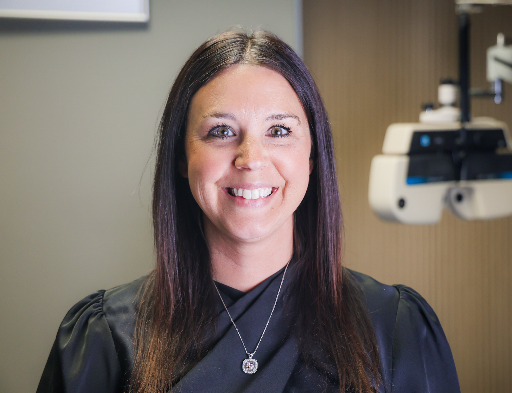 Smiling woman with dark hair in a teal top standing in a bright eyewear store