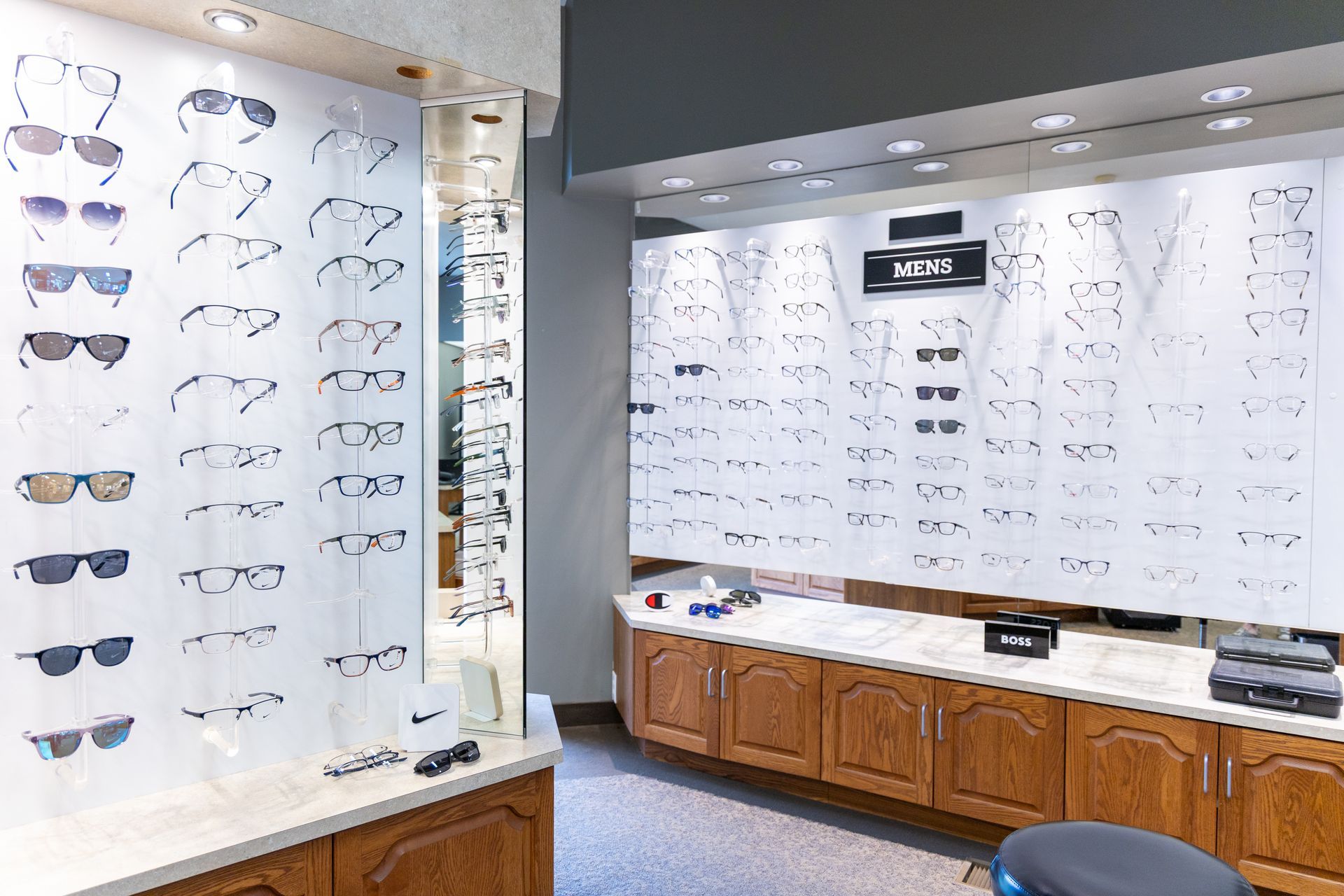 Eyewear store display with rows of eyeglass frames on white wall panels and wood cabinets below