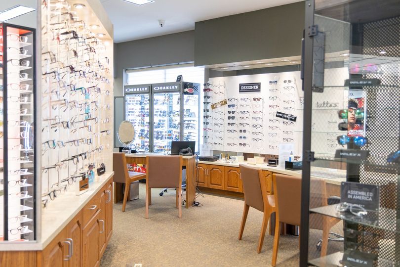 Eyeglass store interior with rows of frames, display cases, and two chairs at fitting tables