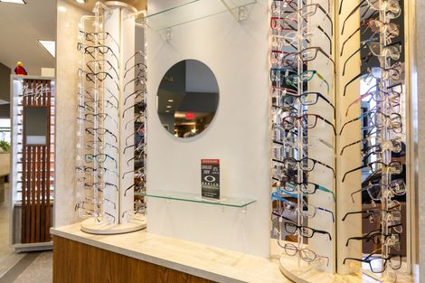 Eyeglasses display in a bright store, with mirrored wall, glass shelves, and rows of frames on both sides
