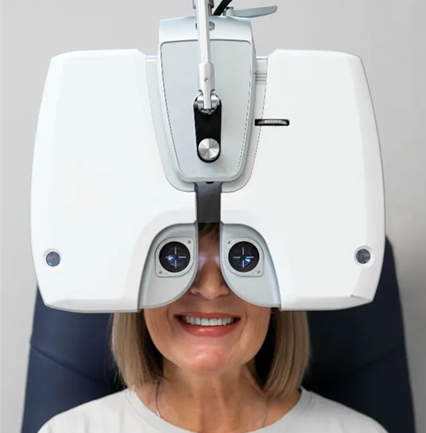 Woman smiling while using an eye exam machine in an optometrist’s office