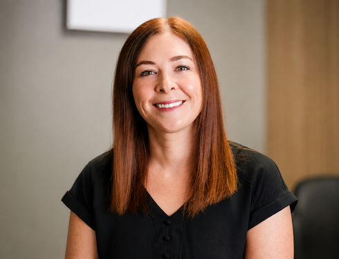 Smiling woman in a teal top standing in an eyeglasses store display area