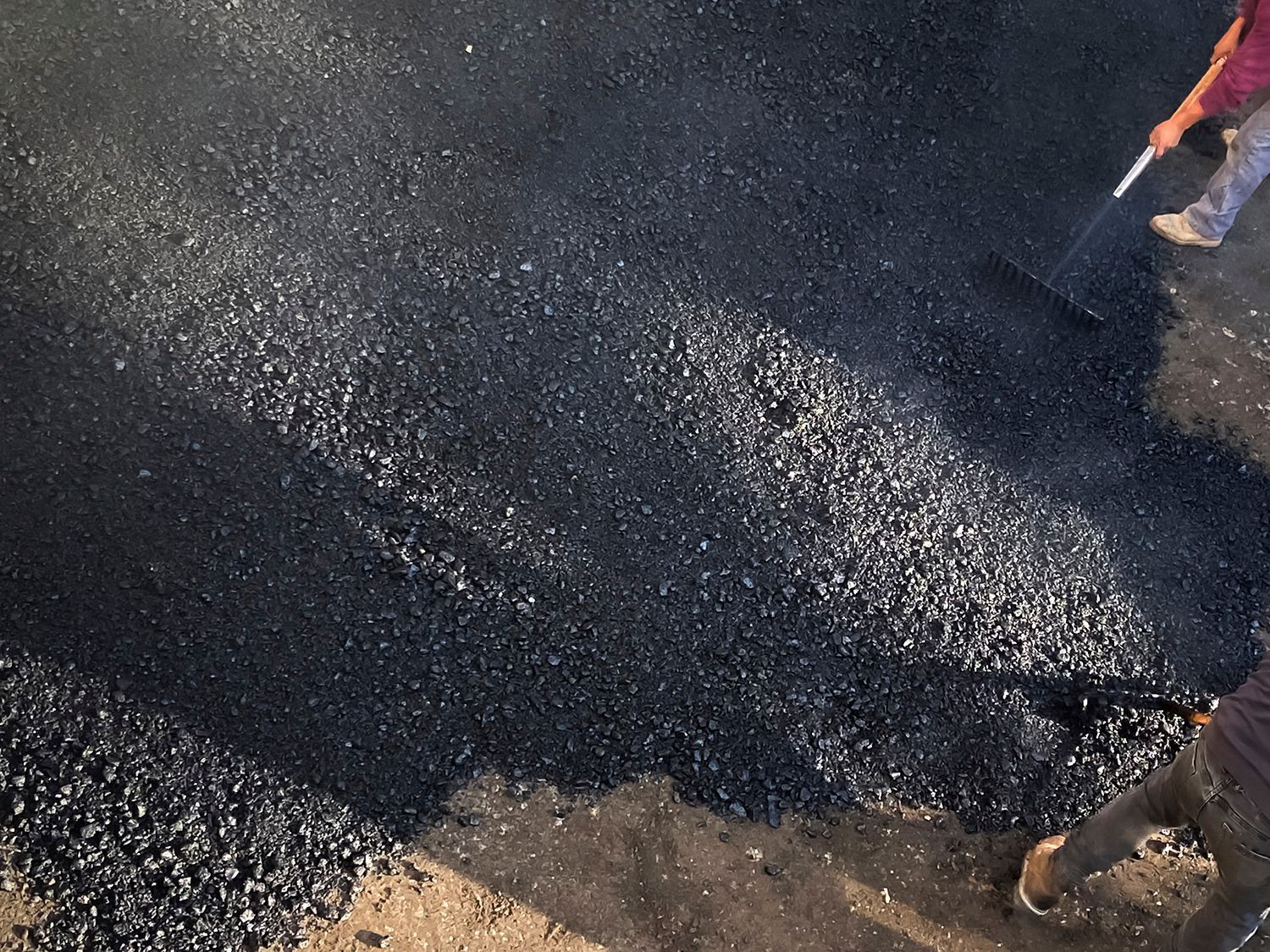 A person is spreading asphalt on the ground with a shovel.