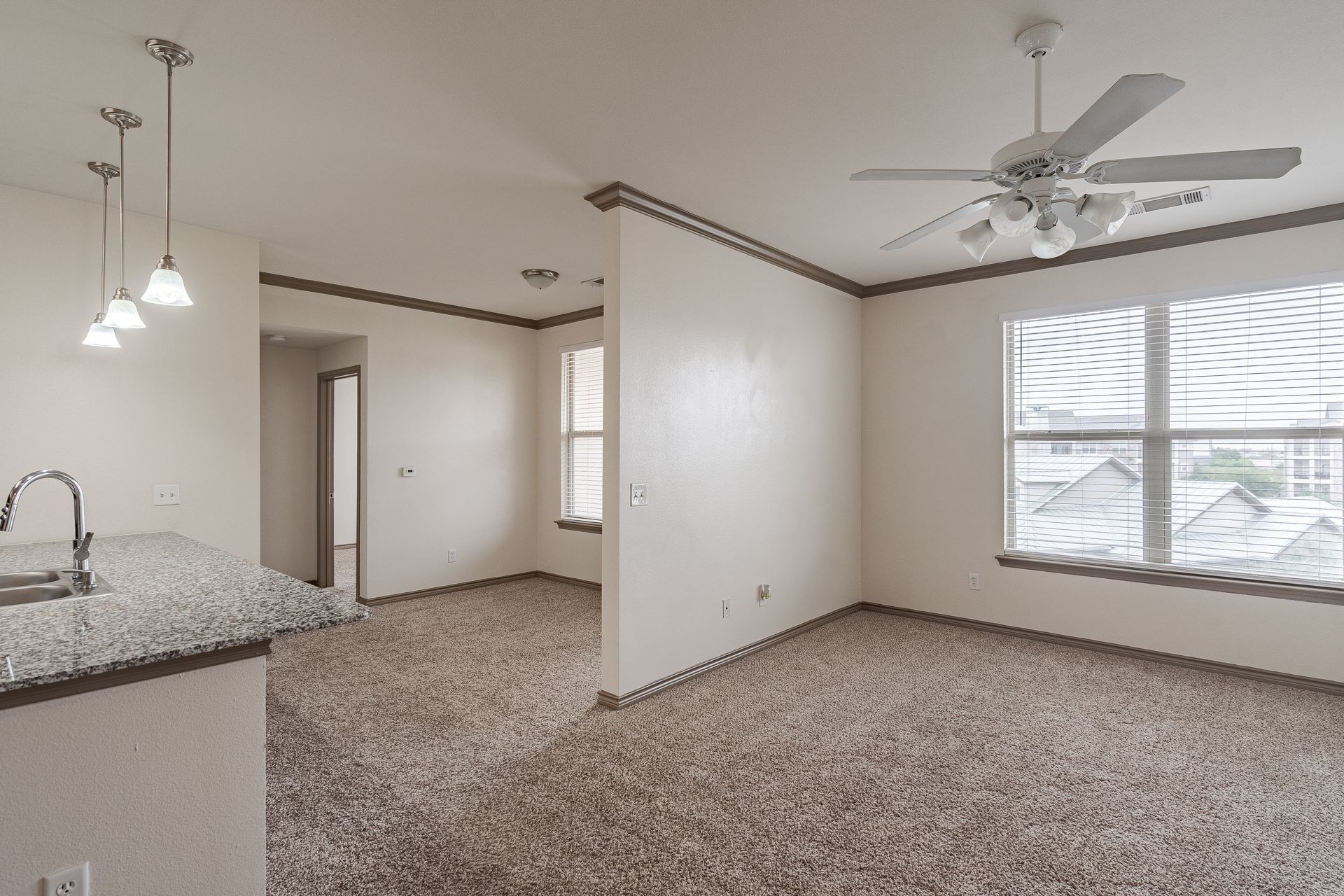 Open-concept living area with granite kitchen island, sink, ceiling fan, and large window.