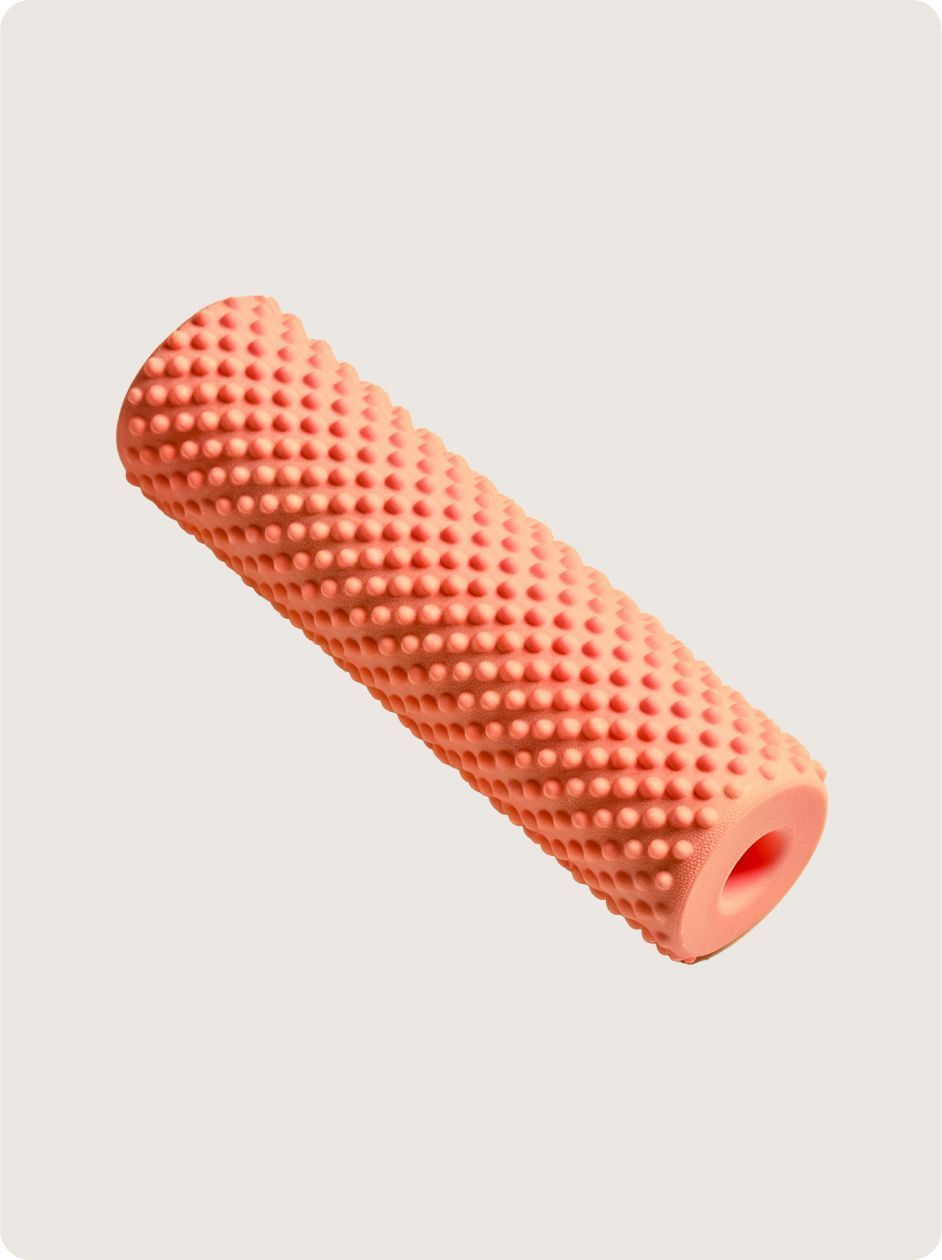 A textured, coral-colored foam massage roller standing at an angle against a plain light-colored background.