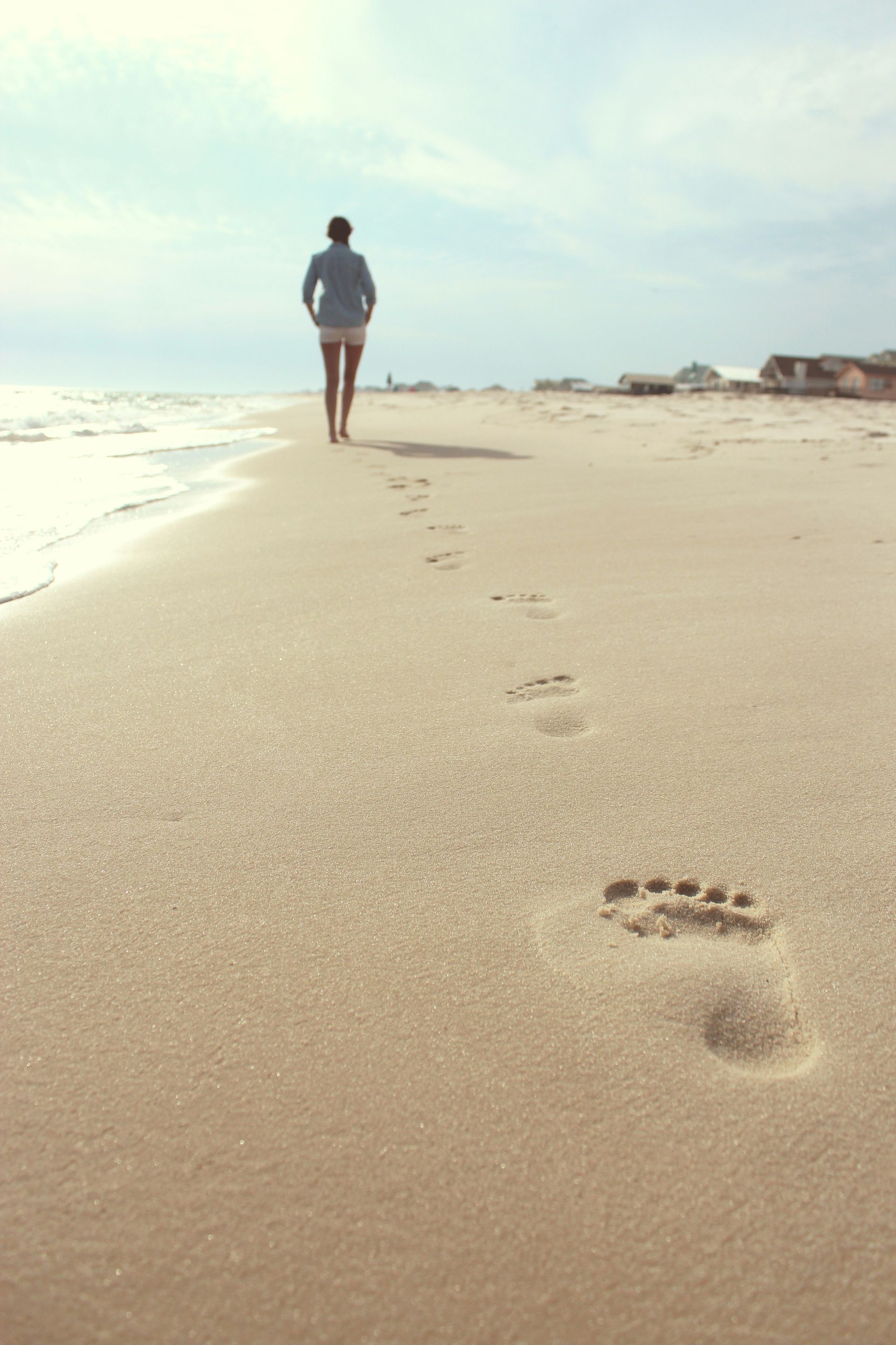 Person walking on a sandy beach, leaving footprints. Ocean in the background, sunny day.