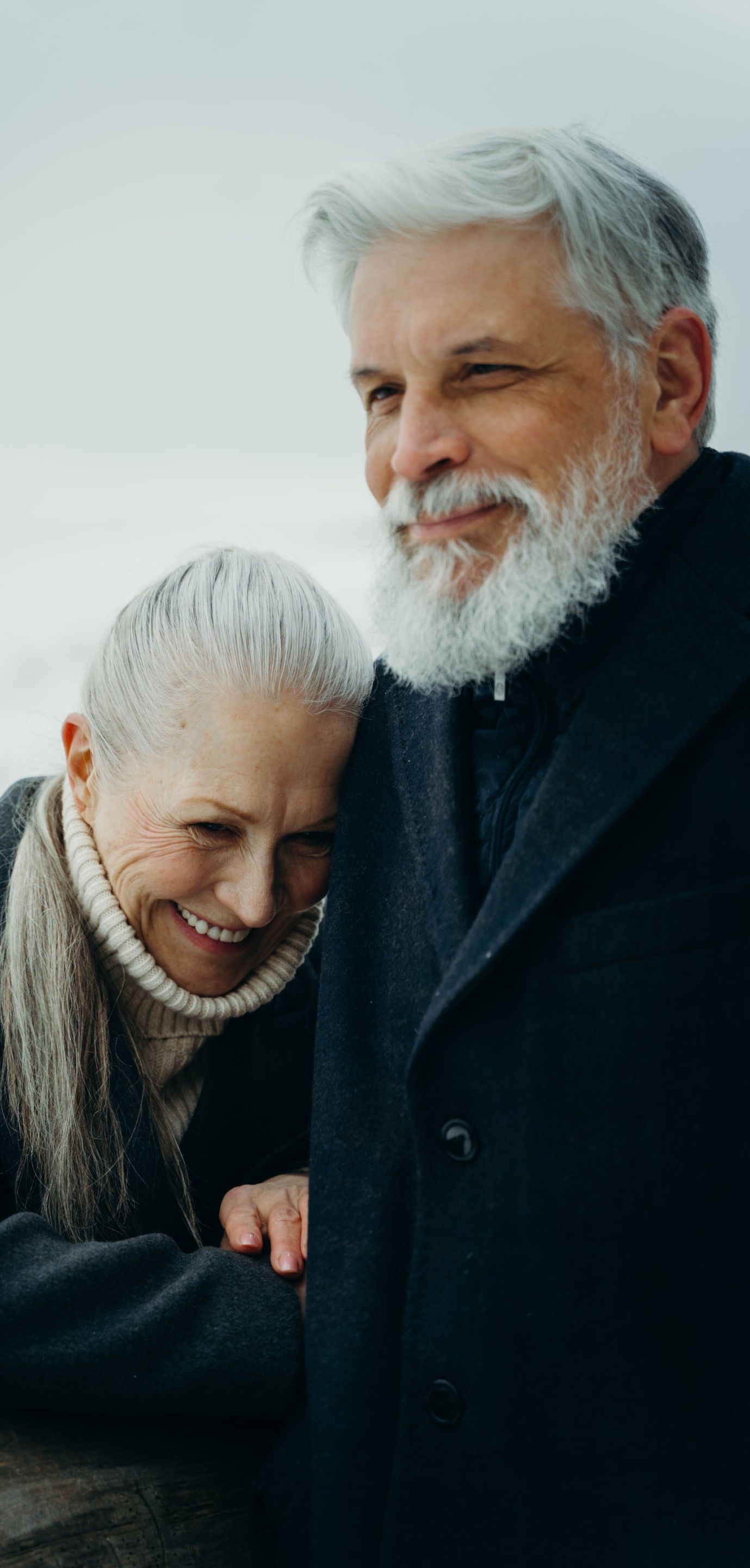 A man with a beard and a woman are hugging each other and smiling.