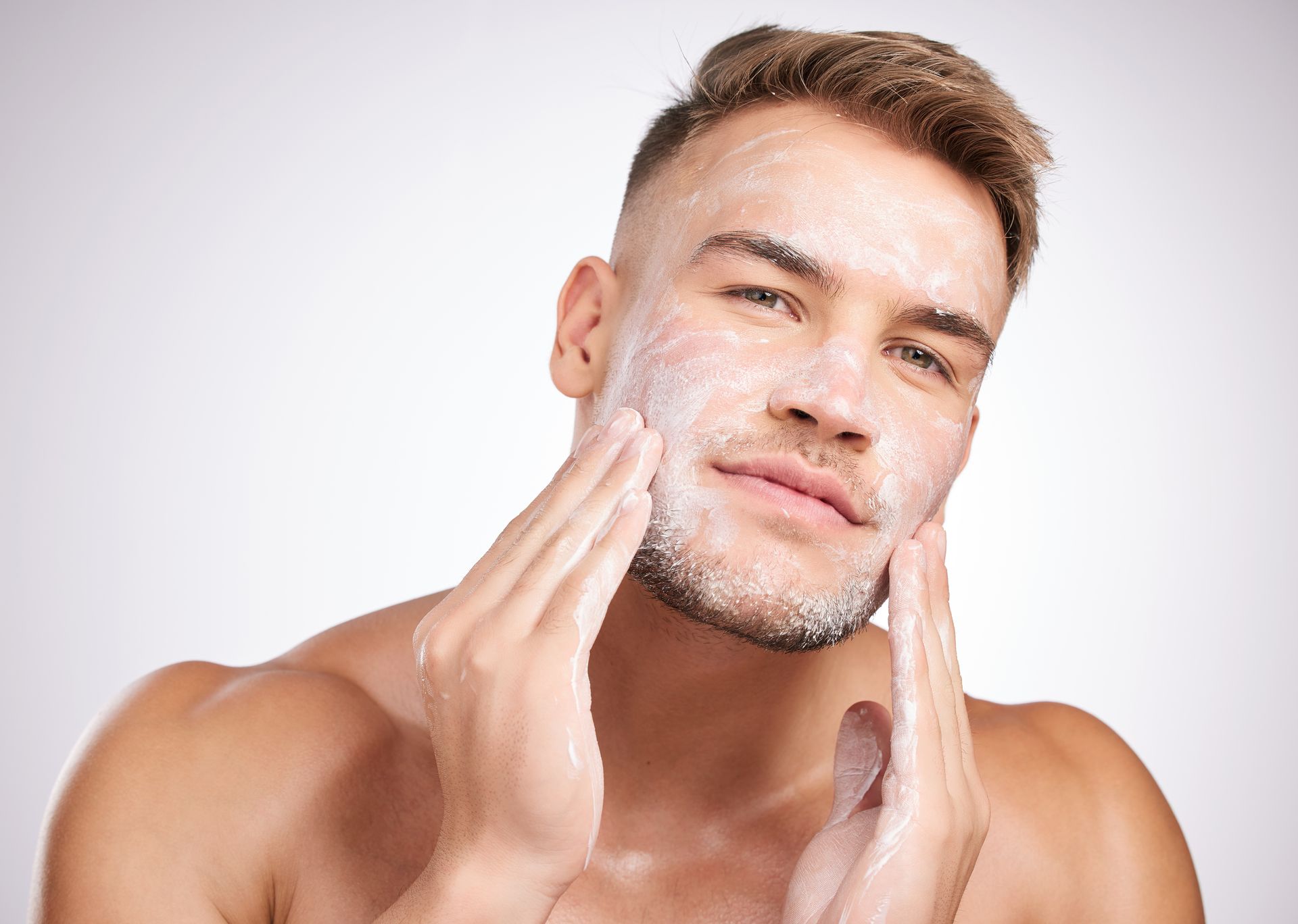 A shirtless man is washing his face with soap.