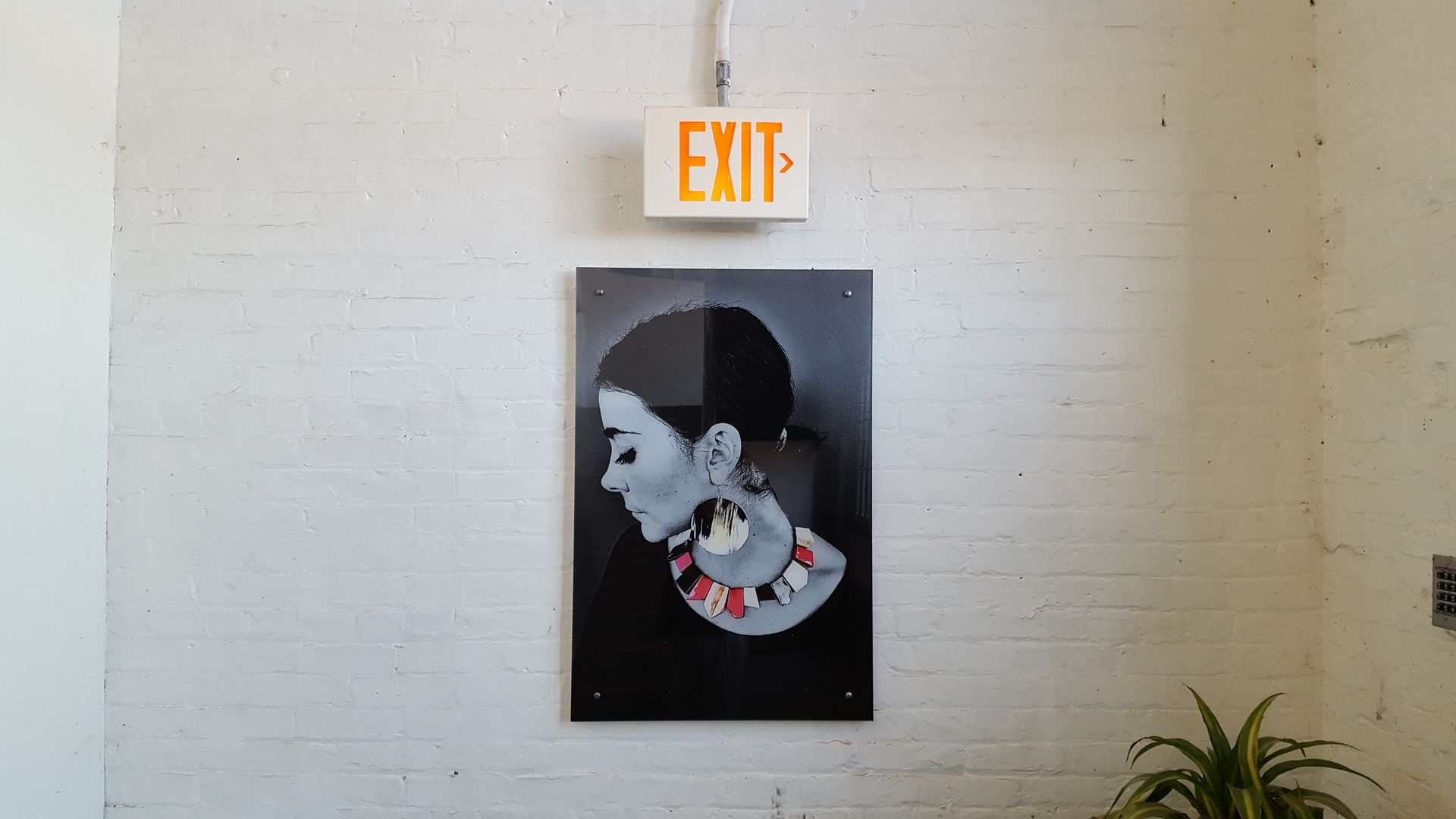 Black-and-white portrait poster beneath an illuminated EXIT sign on a beige wall.
