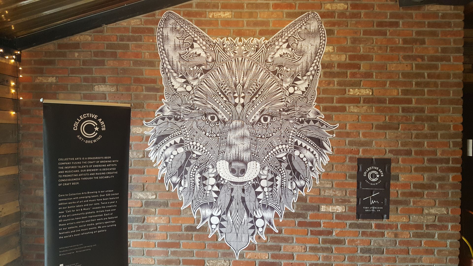 Fox head art on brick wall, with banner and small sign. Black and white, detailed design.
