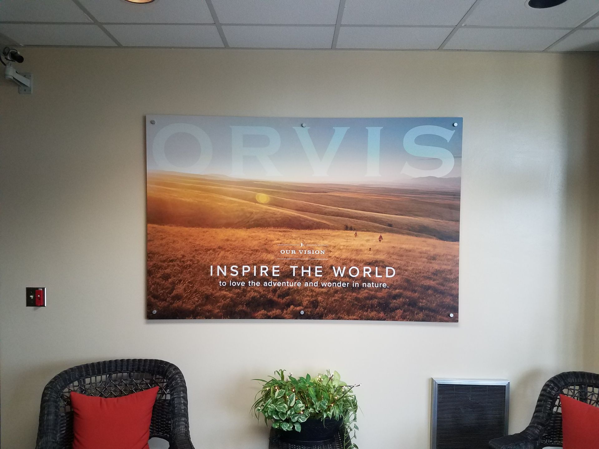 Office lobby with ORVIS poster, two chairs, and a small plant table against beige walls.