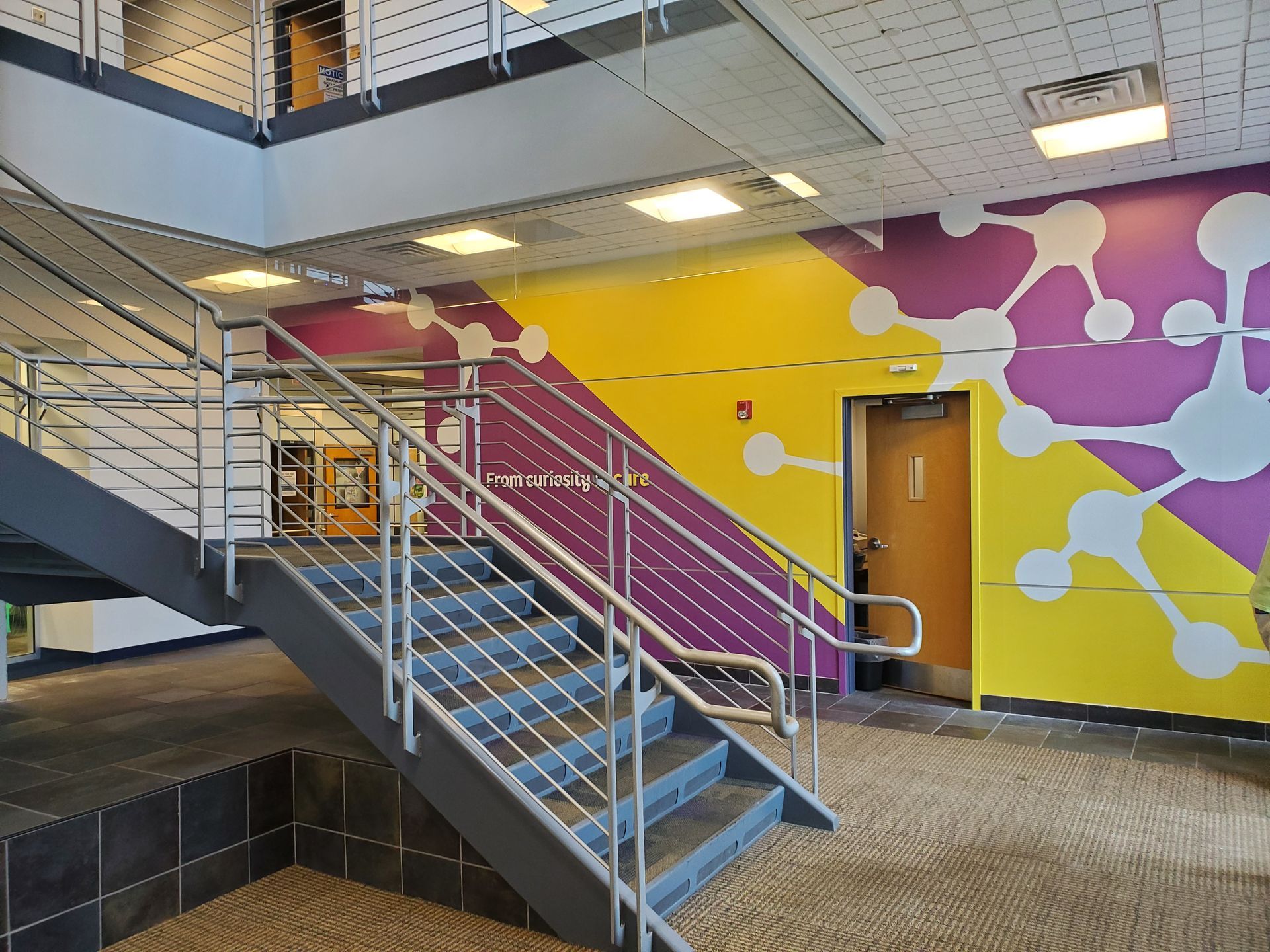 Staircase with metal railings, yellow and purple accent wall with a white molecular design.