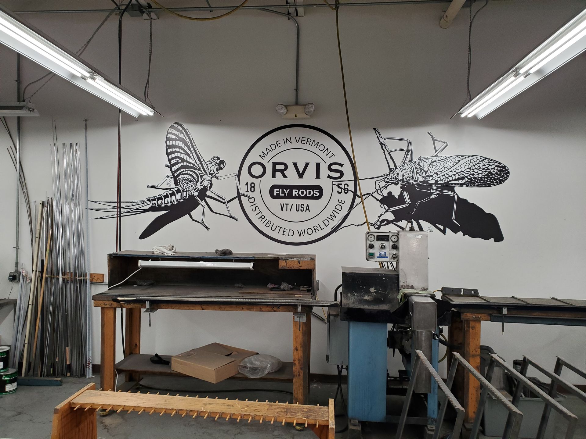 Workshop with an ORVIS logo wall mural, benches, tools, and fluorescent lights.