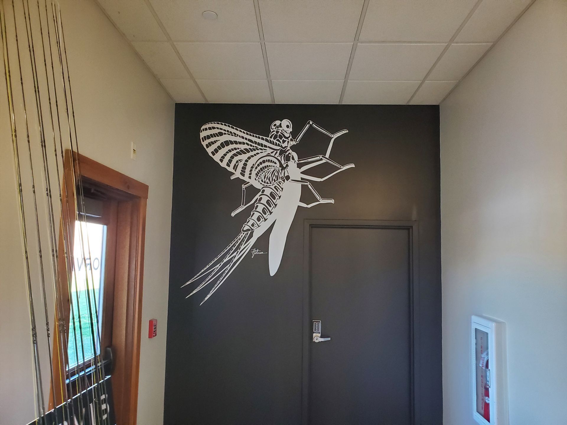 Hallway with a large white mosquito mural above a dark door, with a window on the left.