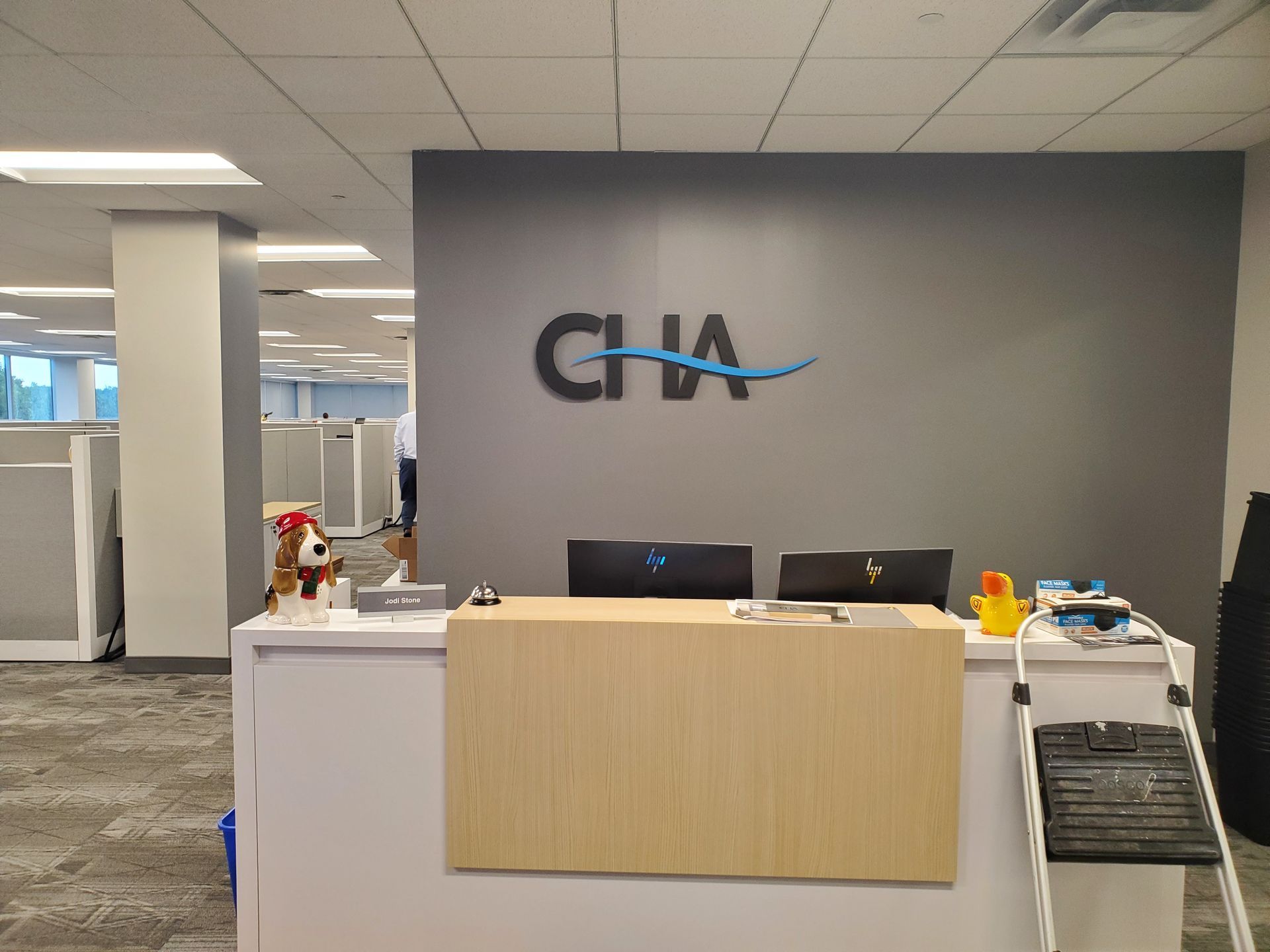 Office reception desk with CHA logo on a gray wall, in an open-plan workspace