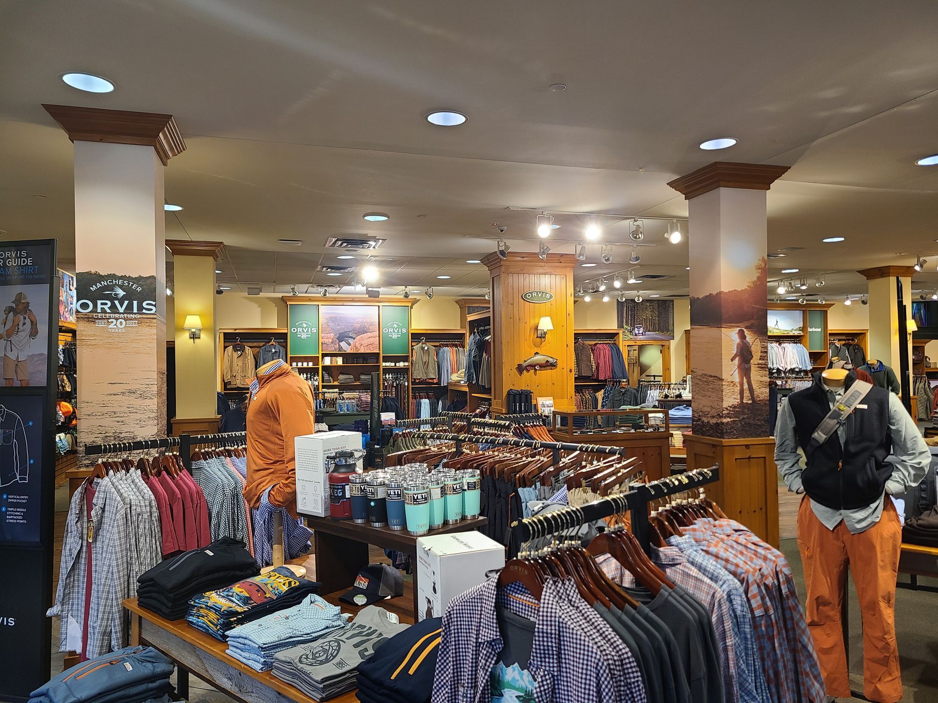 Clothing store interior with racks of shirts and jackets, bright ceiling lights, and two shoppers browsing.