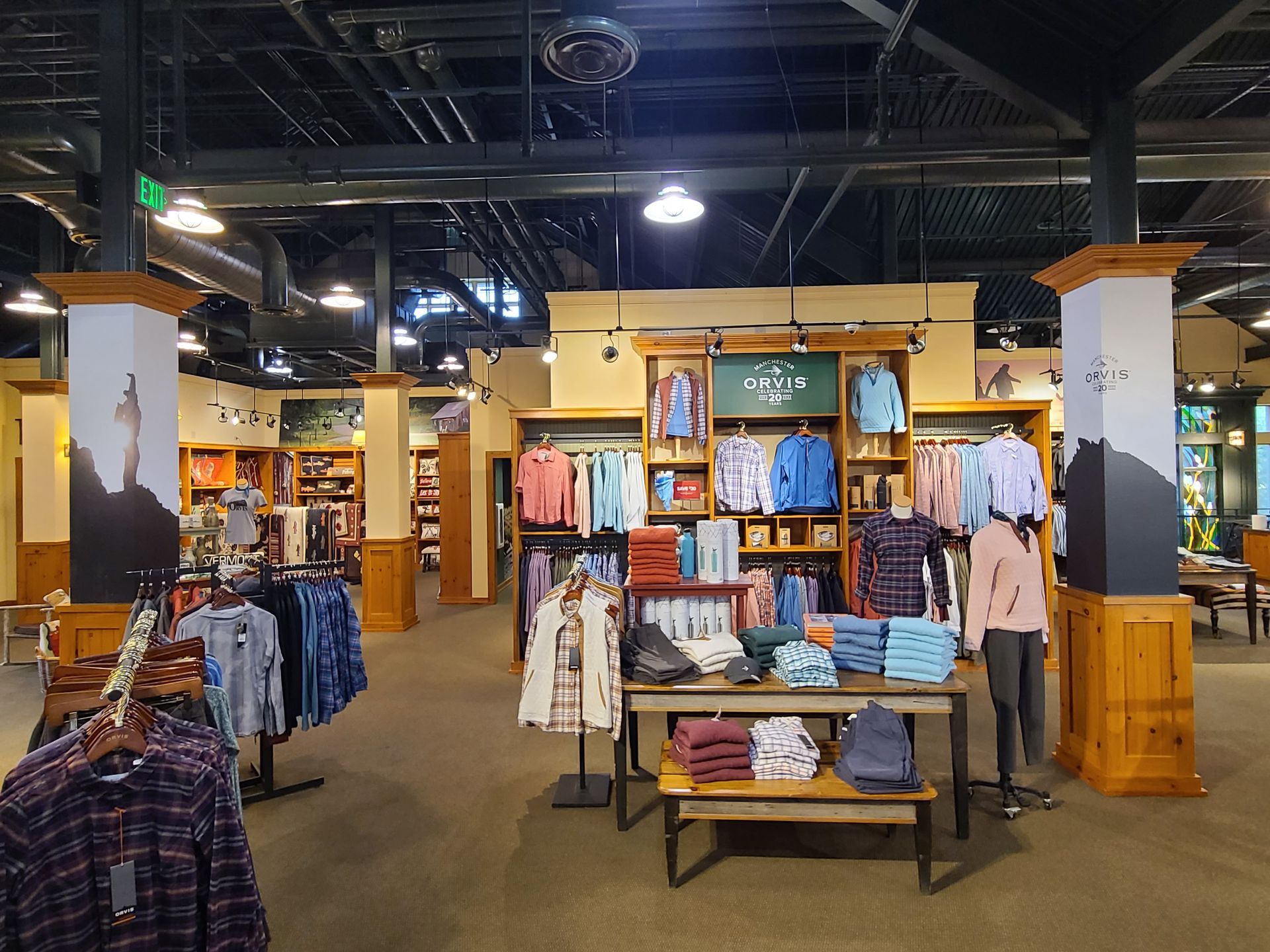 Clothing store interior with folded shirts, racks of apparel, and wooden display shelves under bright lights